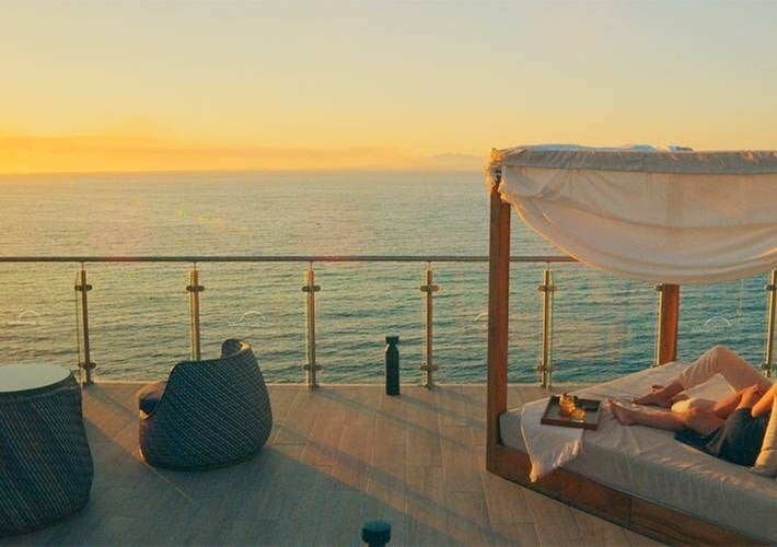 a person is laying on a canopy bed on a balcony overlooking the ocean