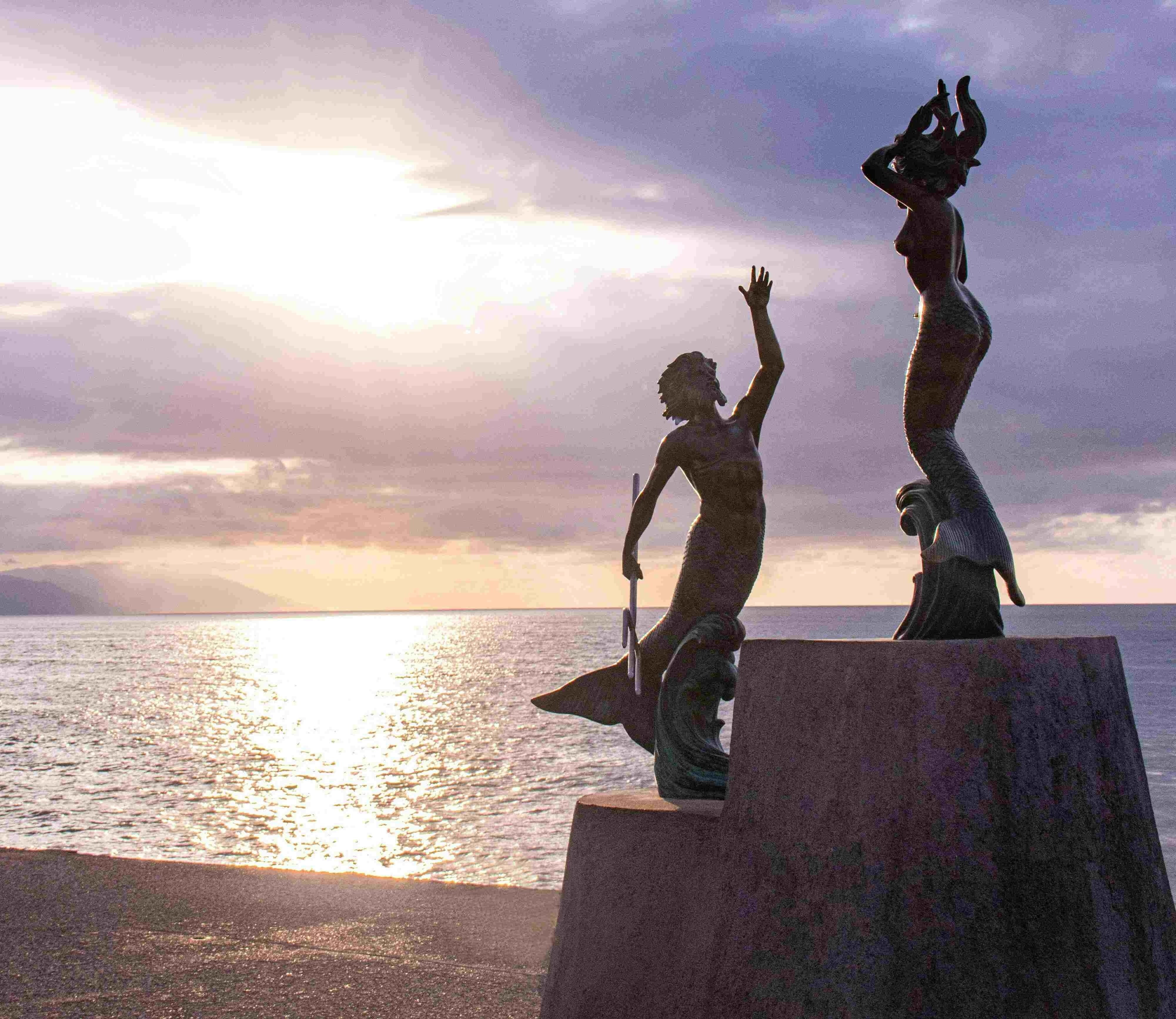 duas estátuas de sereia ao lado do oceano ao pôr do sol