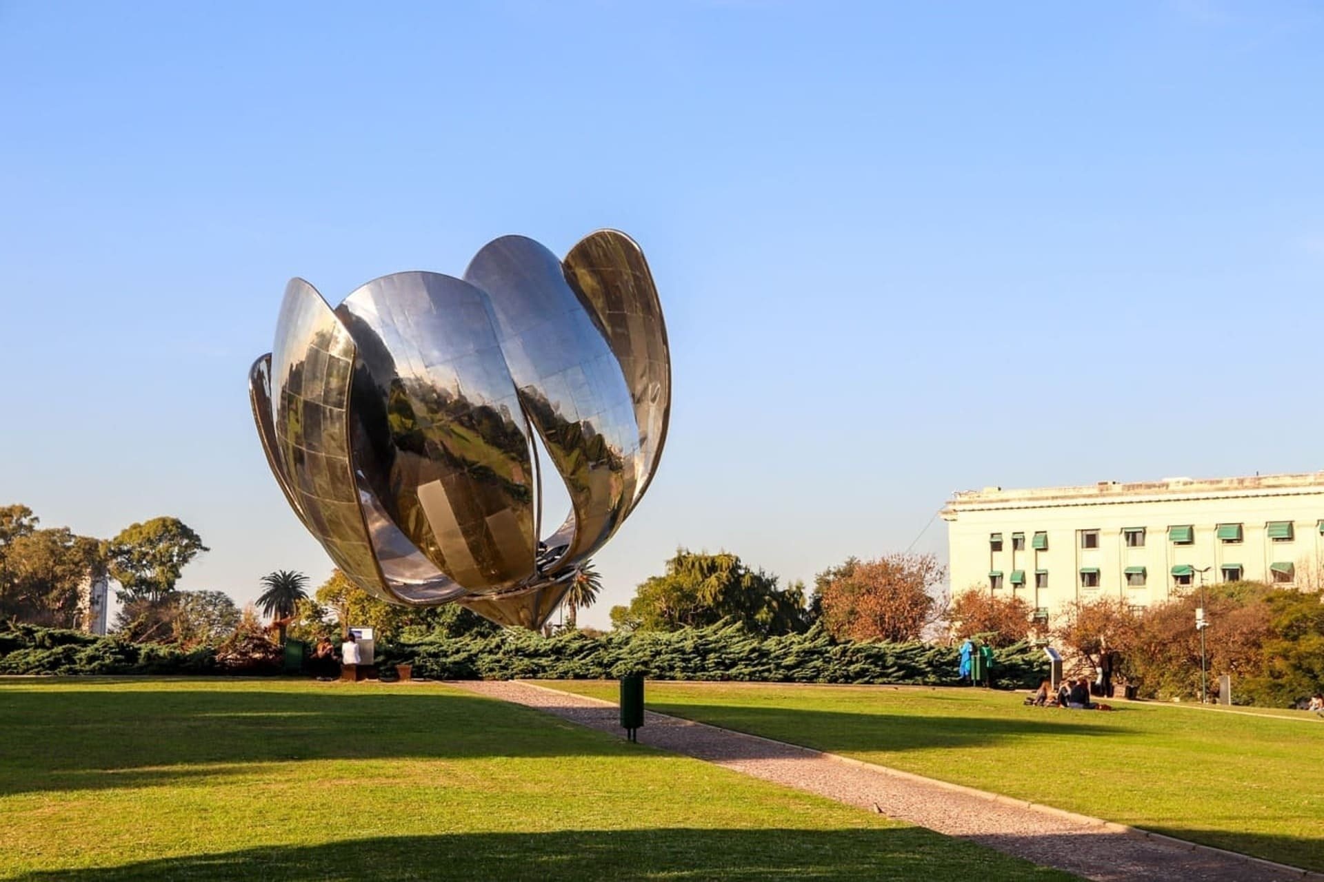 a large silver sculpture in a park with a building in the background