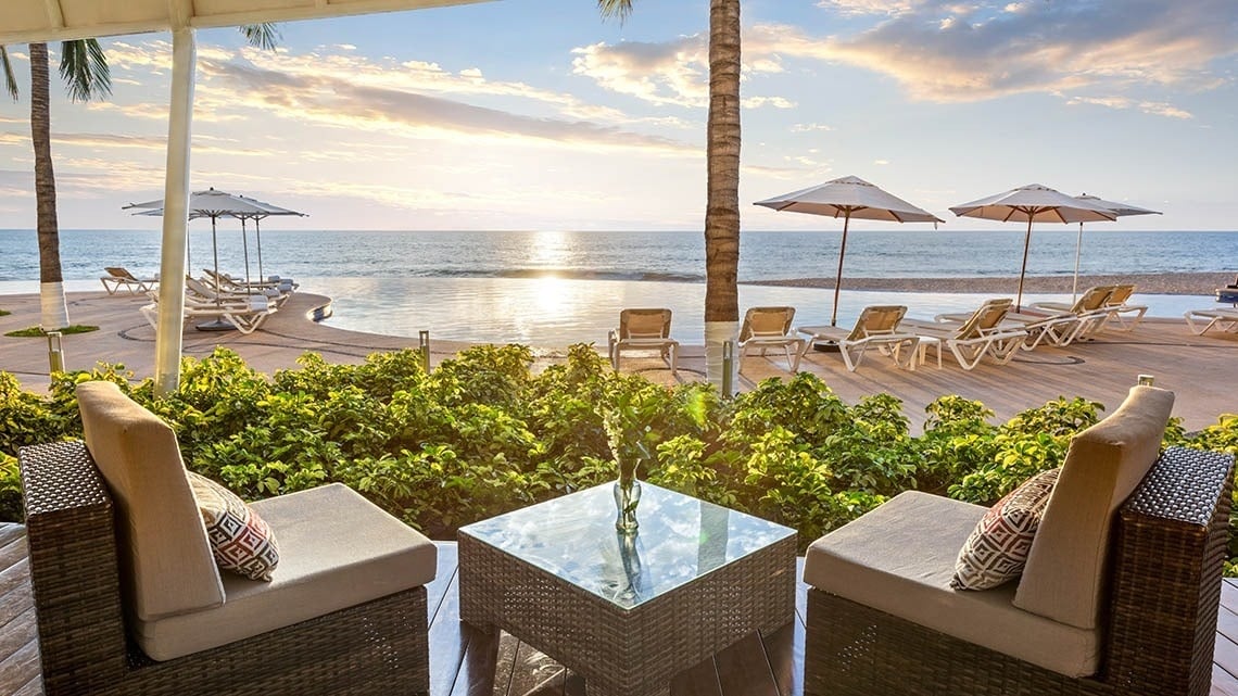 a view of the ocean from a patio with chairs and umbrellas