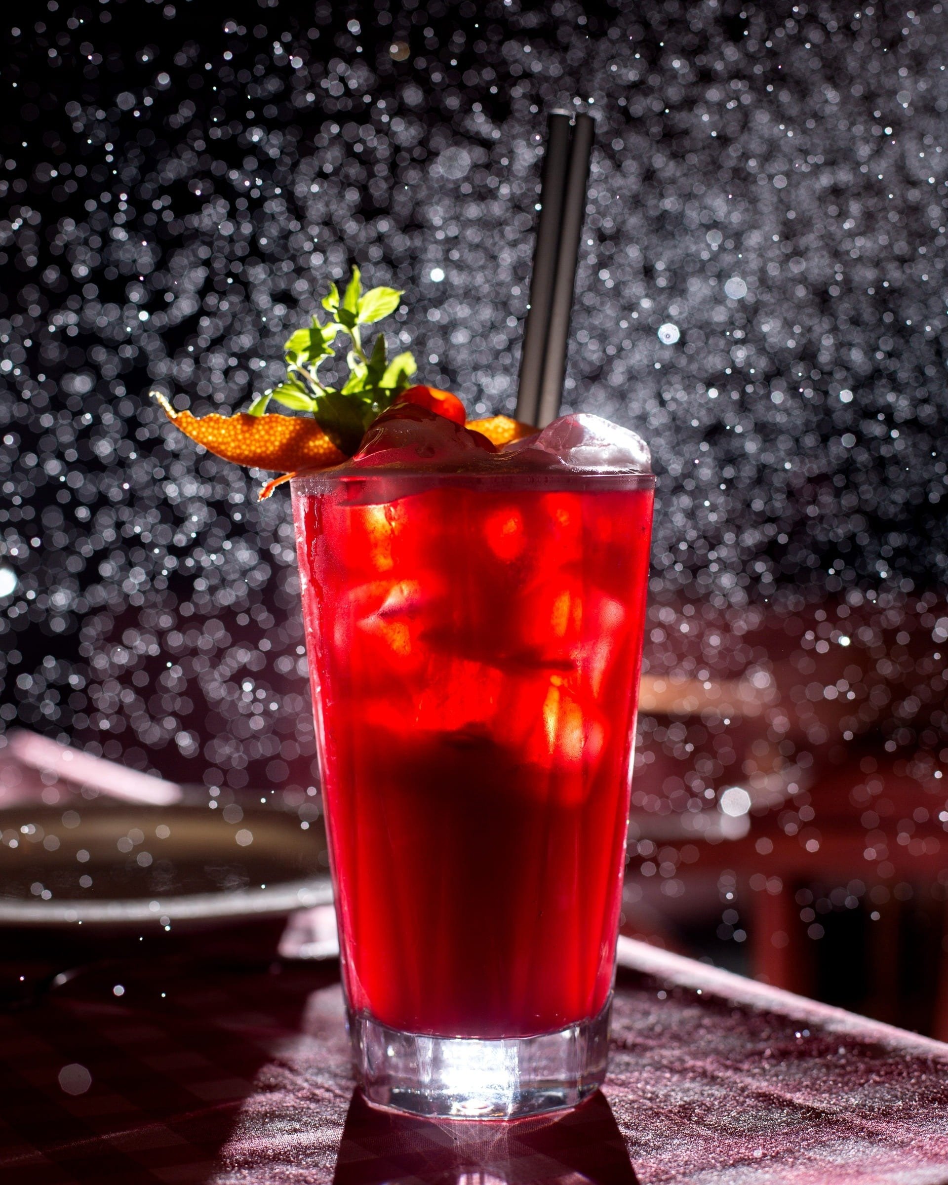 a tall glass of red liquid with ice and a straw