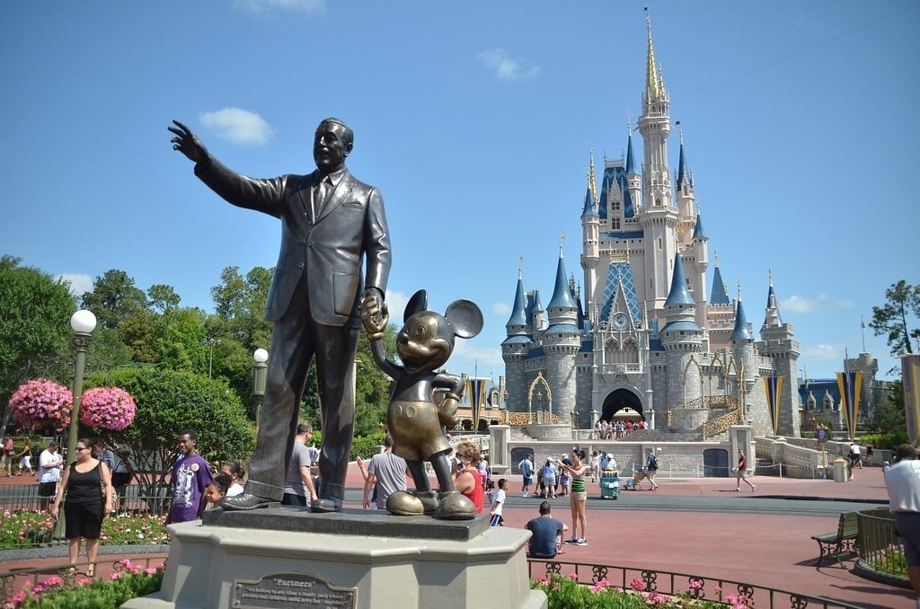 a statue of walt disney and mickey mouse in front of cinderella castle