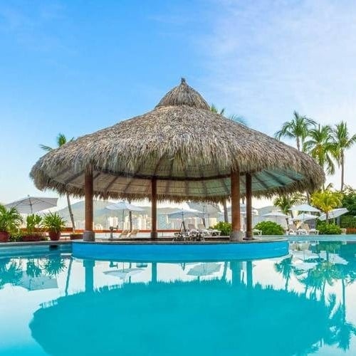 Bar com telhado de palmeira em uma piscina externa no Park Royal Beach Acapulco Hotel