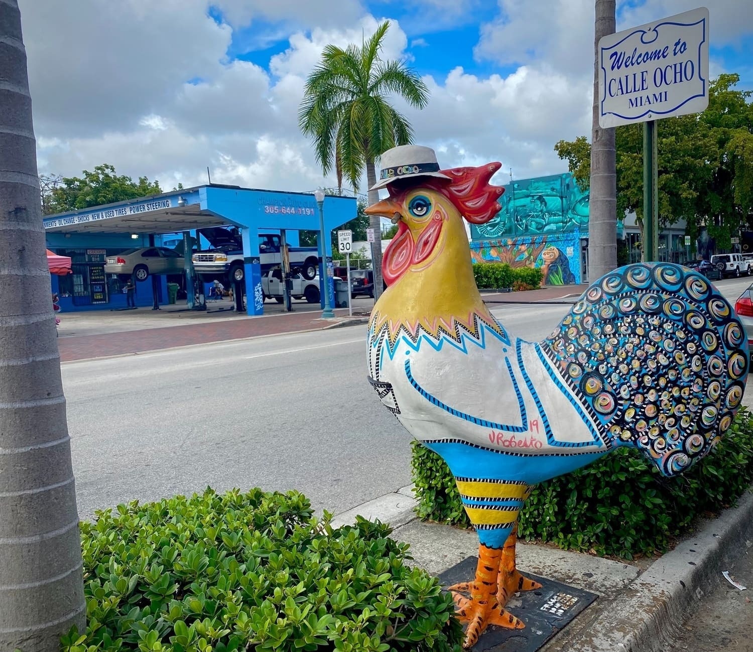 a statue of a colorful rooster in front of a welcome to calle ocho miami sign