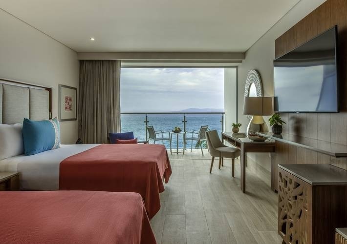 a hotel room with two beds and a balcony overlooking the ocean