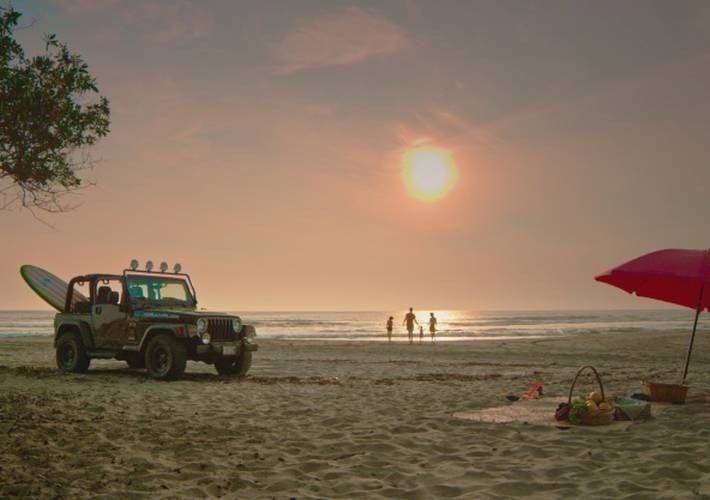 a jeep is parked on the beach with a surfboard on top