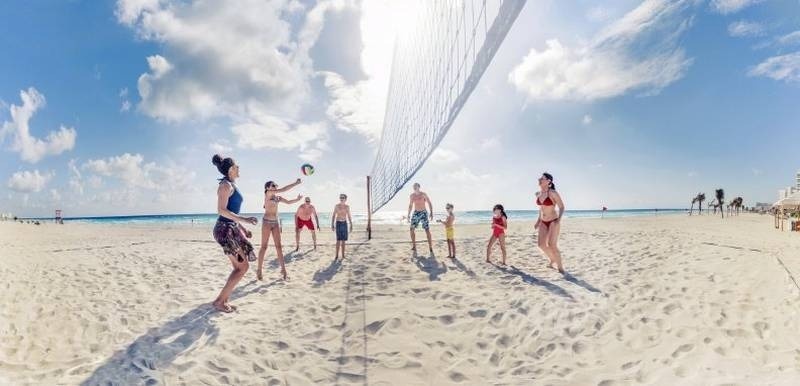 Familia y grupo de amigos jugando al voleibol en la playa del Hotel Park Royal Beach Cancún