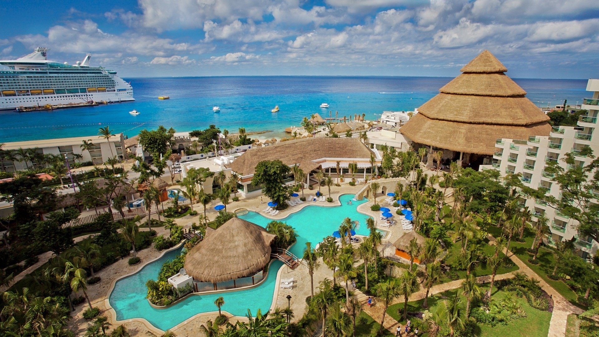 an aerial view of a tropical resort with a cruise ship in the background