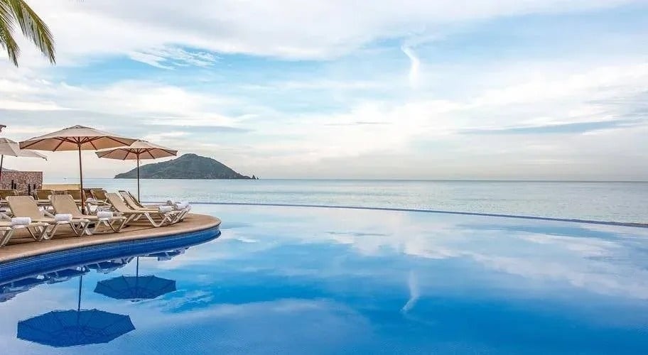 an infinity pool surrounded by chairs and umbrellas overlooking the ocean .