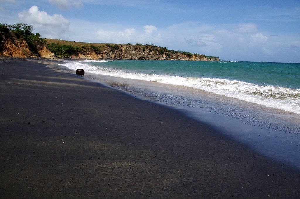 una playa con arena negra y olas en un día soleado