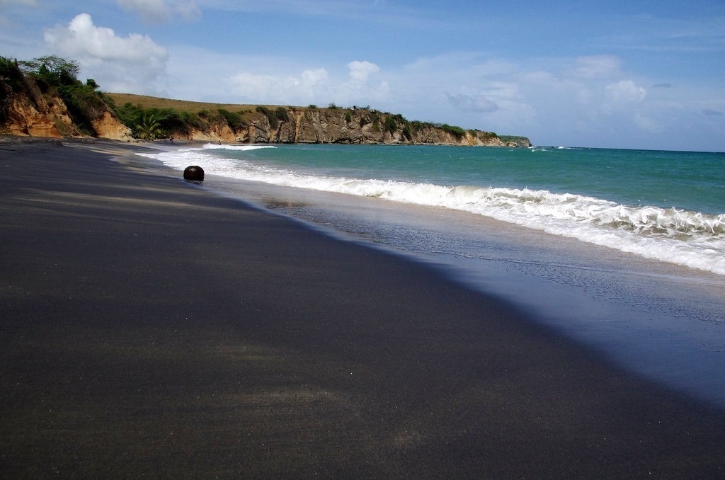 a black sandy beach with a cliff in the background