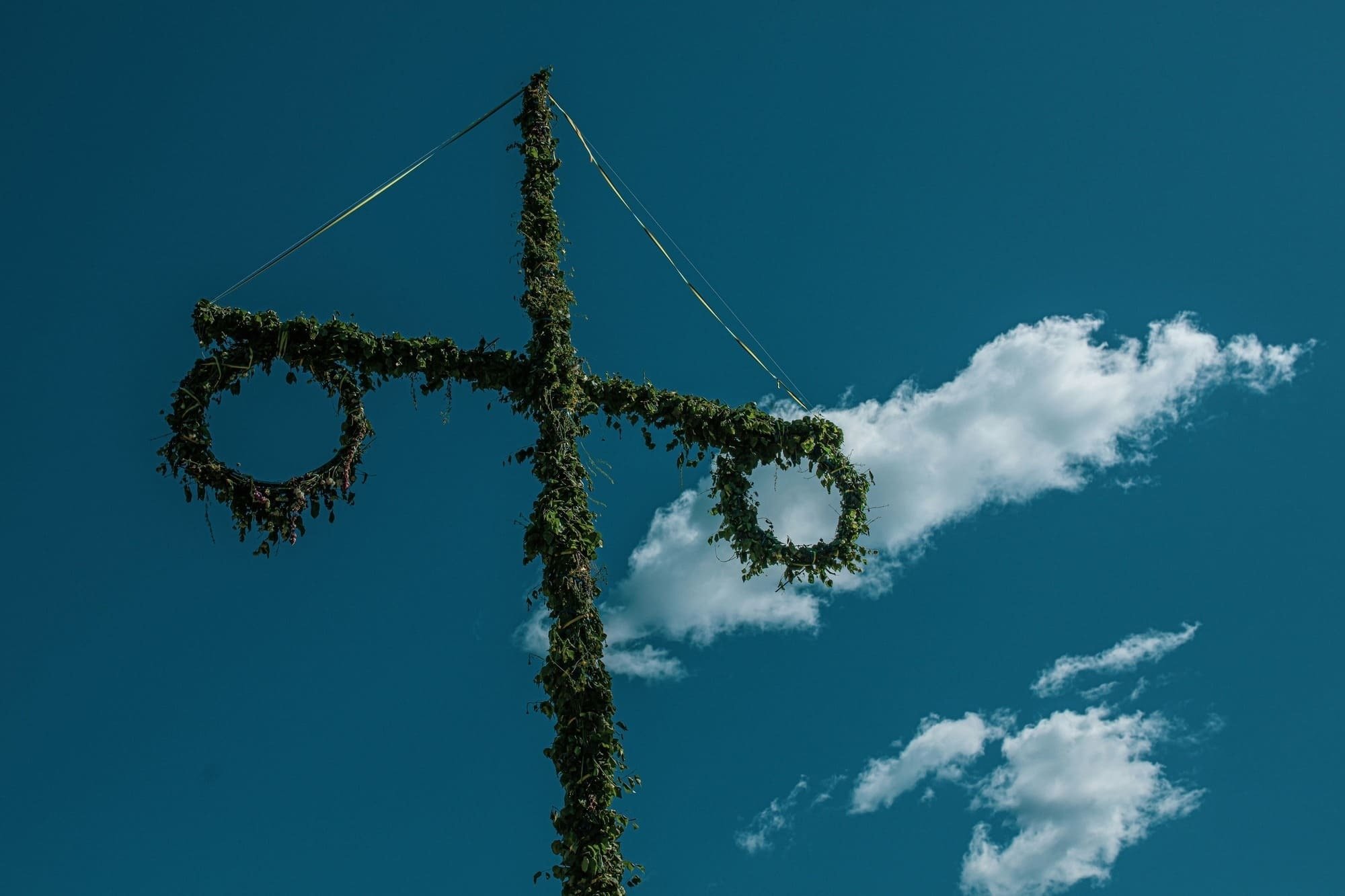 uma cruz decorada com coroas de flores e folhas contra um céu azul