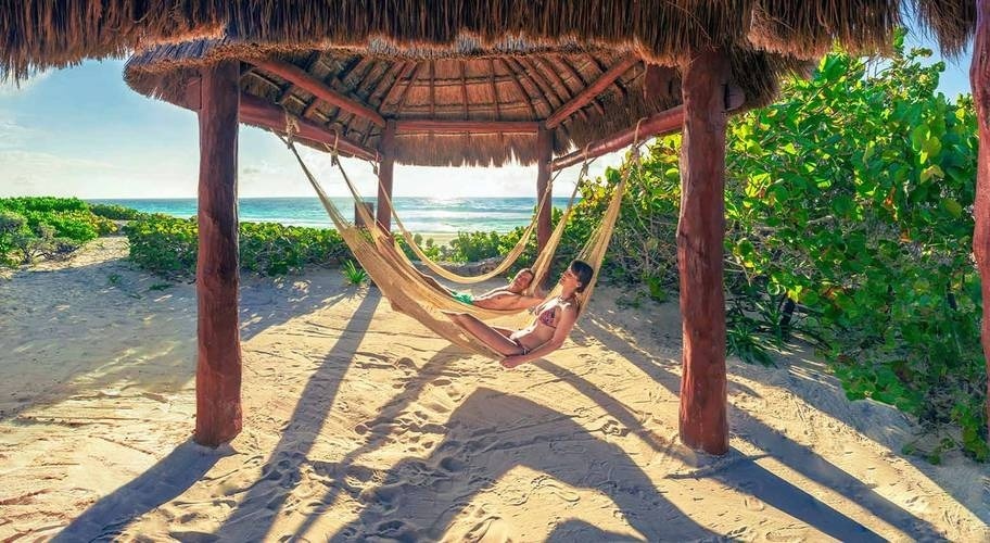 Casal descansando em redes sob um telhado de palmeira na praia do Hotel Park Royal Beach Cancun