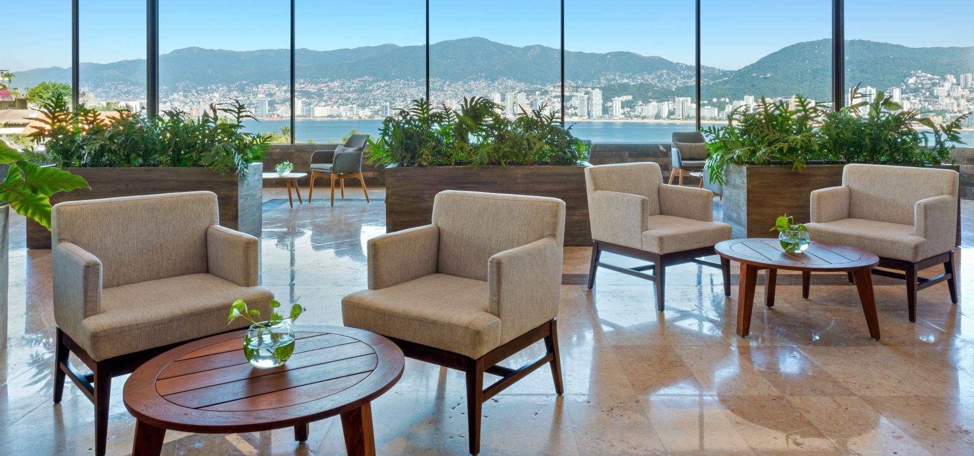 Área de relaxamento com mesas e poltronas, decorada com cores cruas e madeira com vista para o mar no Hotel Park Royal Beach Acapulco