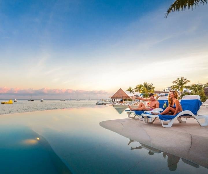 Pareja en hamaca cerca de piscina infinity con vistas al mar en el Hotel Grand Park Royal Cozumel