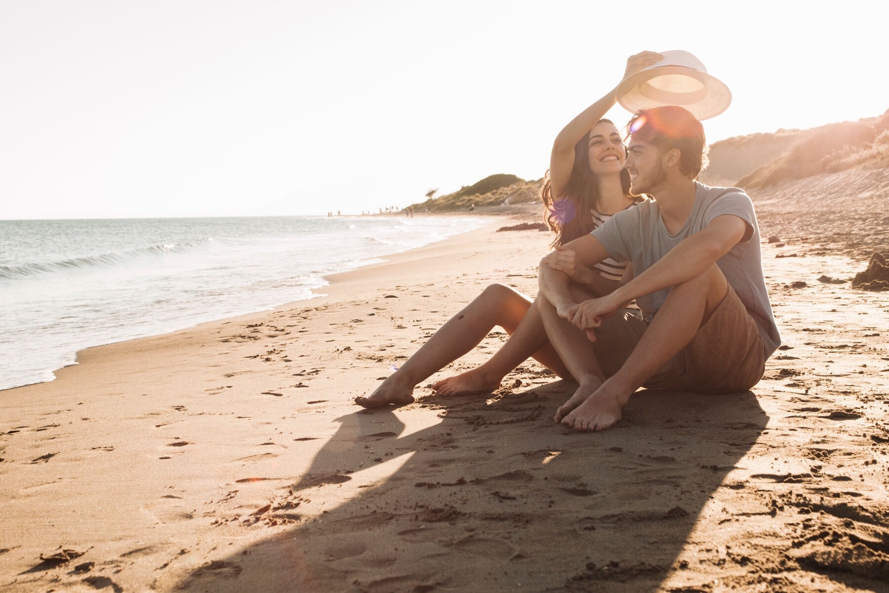 a man and woman are sitting on the beach looking at the ocean