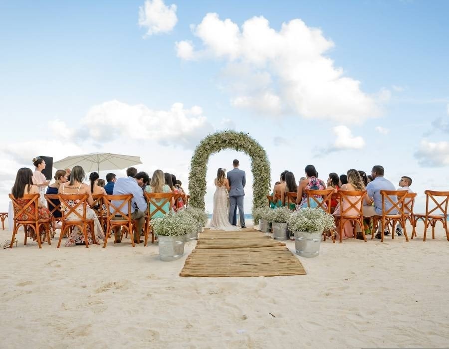 Novios en altas, con invitados sentados en sillas en la playa, Park Love de  Park Royal hotels and resorts 