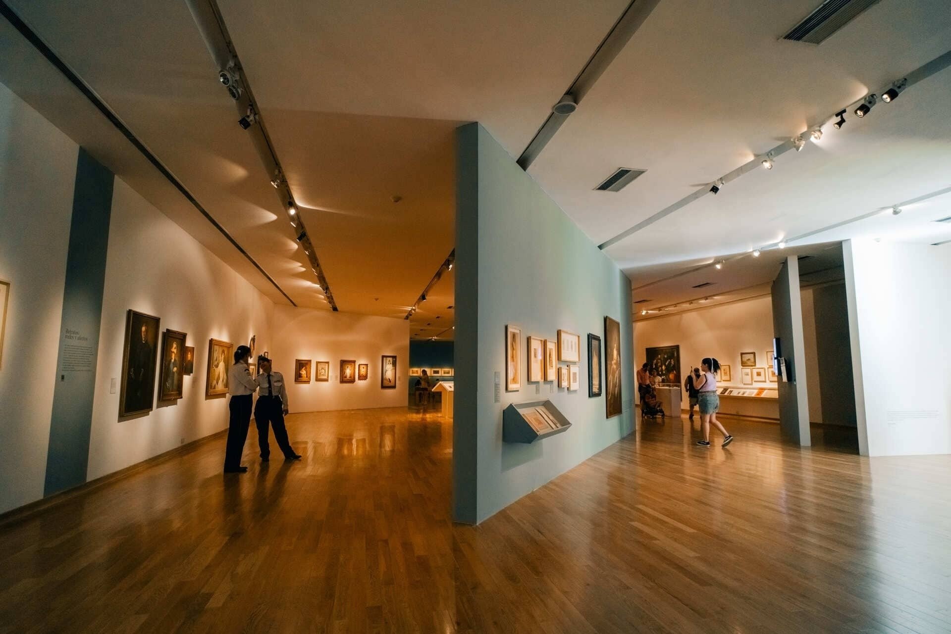 people looking at paintings in a museum with a sign that says ' paintings ' on it