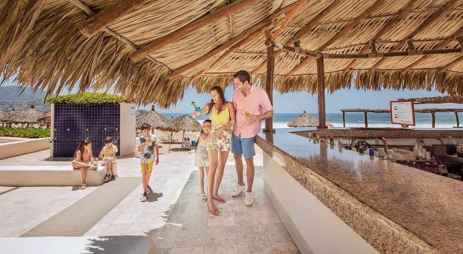 Familia comiendo un snack en un bar con techo de palma en Park Royal Beach Ixtapa, México