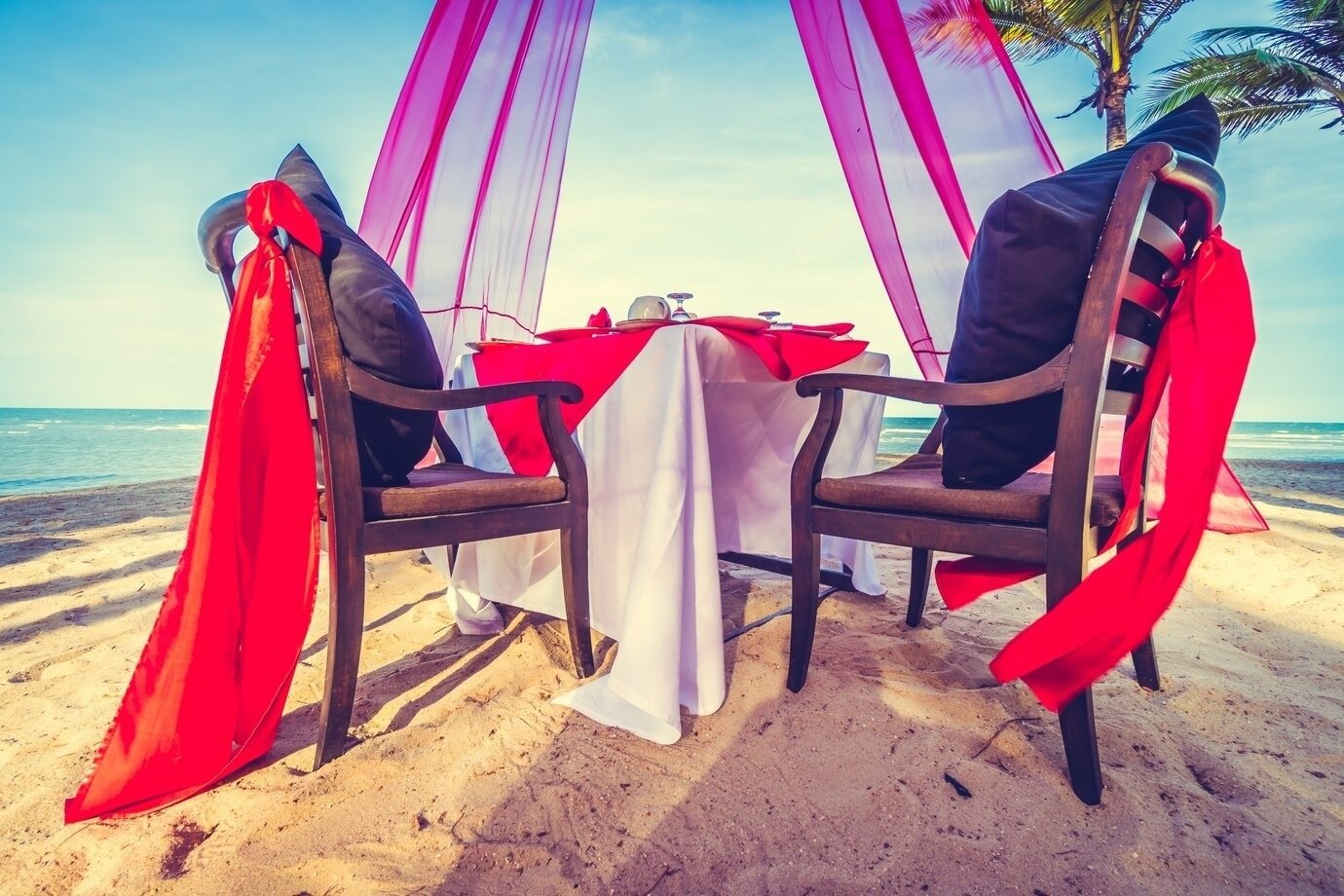 a table and chairs on the beach with red ribbons