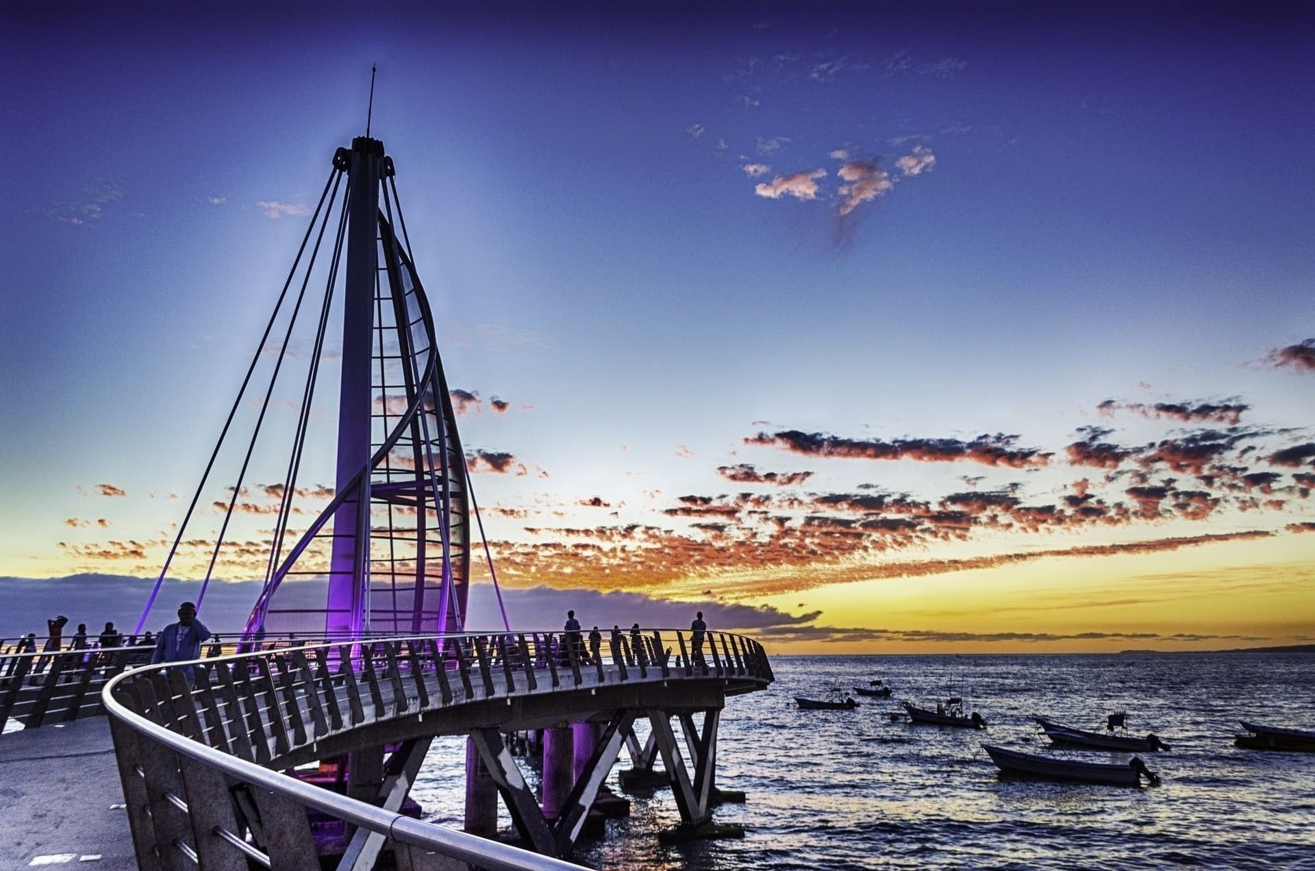 uma ponte sobre o oceano ao pôr do sol com barcos ao fundo