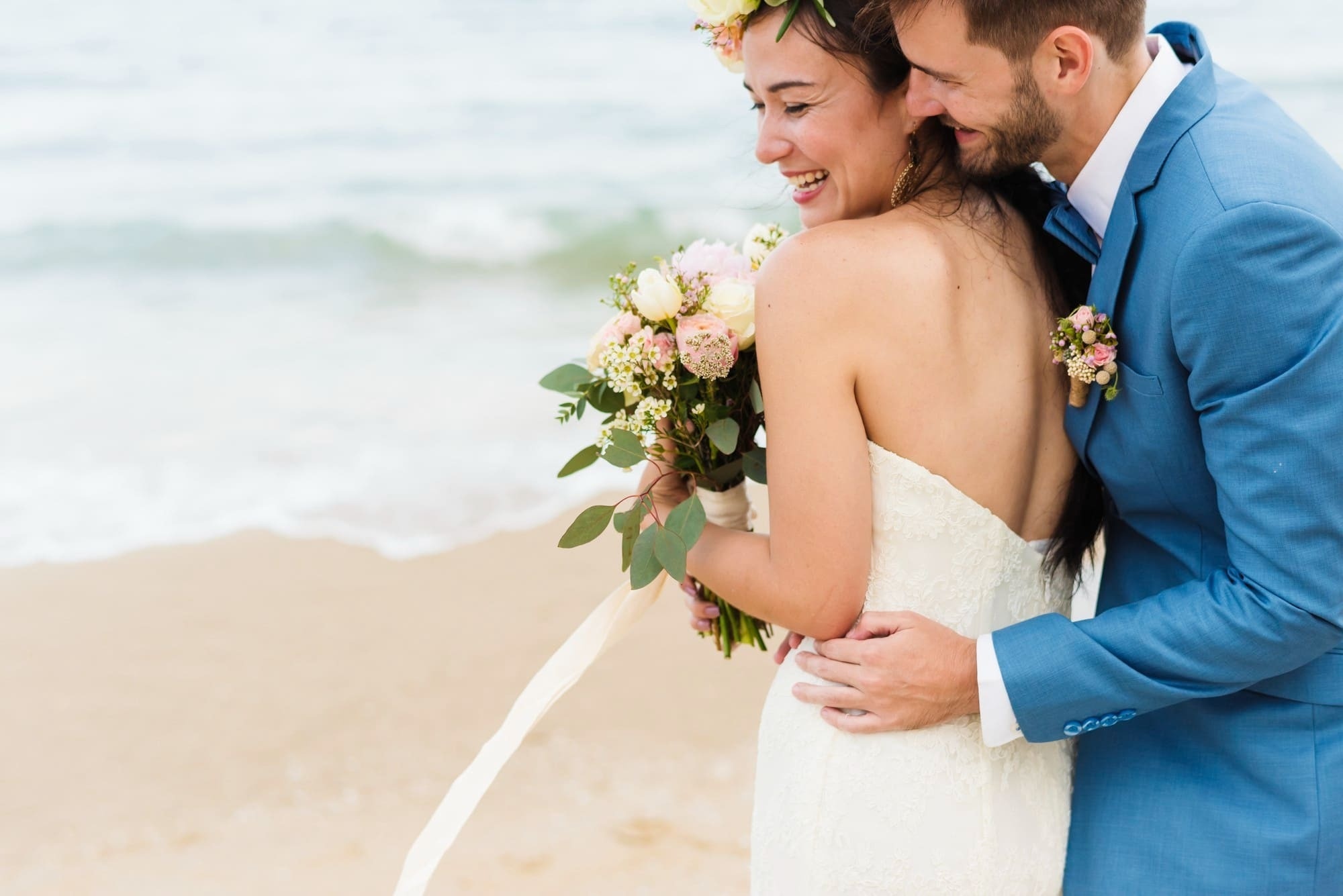 a bride and groom on the beach with the bride holding a bouquet of flowers