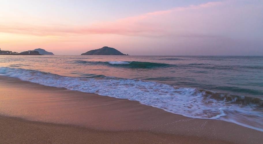 Pôr do sol sobre uma praia com areia dourada e água turquesa no México