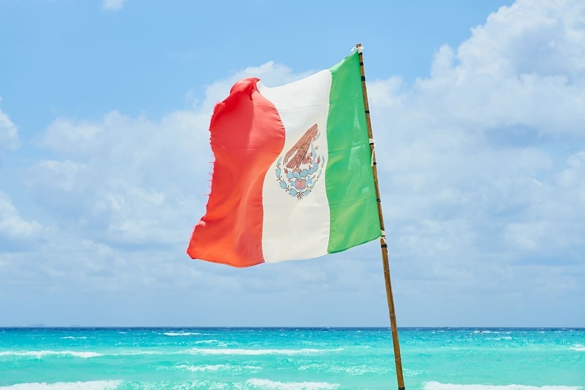 a mexican flag is waving in the wind on a beach