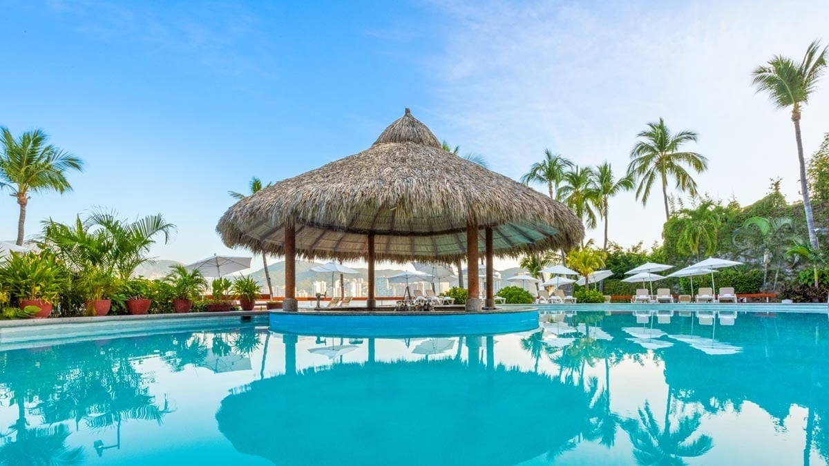 Coco Bar con tejado de palma junto a una piscina exterior del Hotel Park Royal Beach Acapulco
