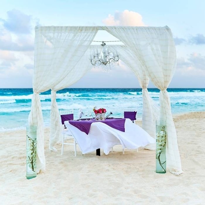 Mesa de casamento sob pérgola de tecido branco com lustre à beira-mar, Cancun no México