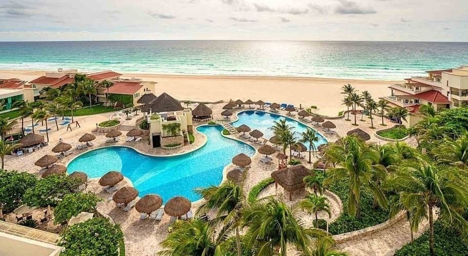 an aerial view of a resort with a large swimming pool surrounded by palm trees and chairs .