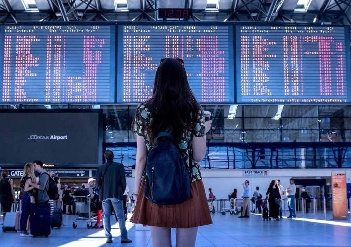 a woman with a backpack stands in front of a large sign that says departures