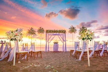 a wedding ceremony is taking place on the beach at sunset .