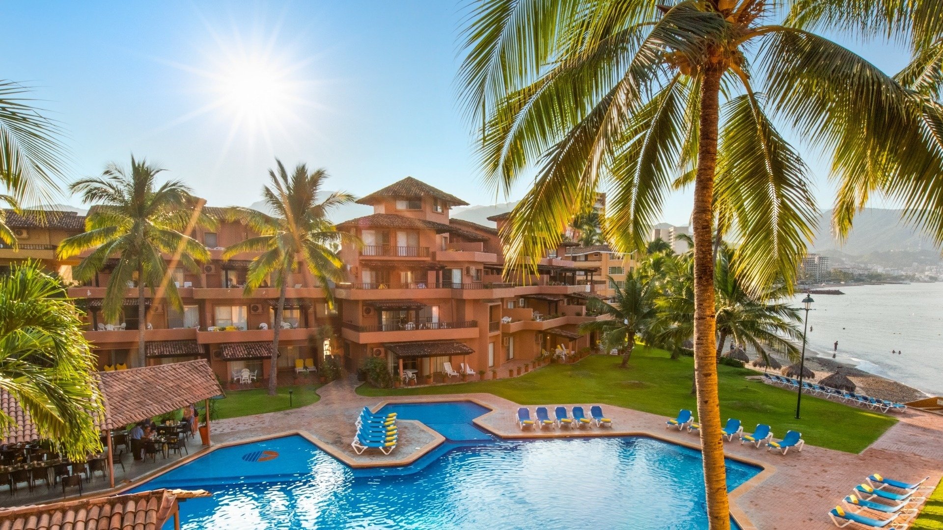 a large swimming pool surrounded by palm trees in front of a hotel