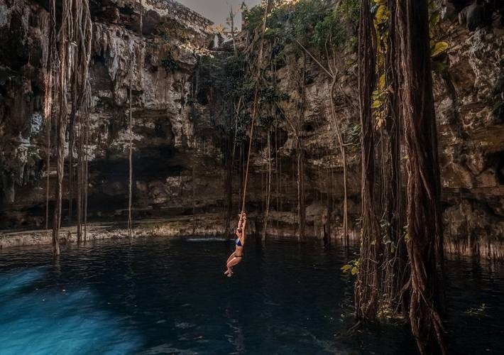 a woman is hanging from a rope over a body of water