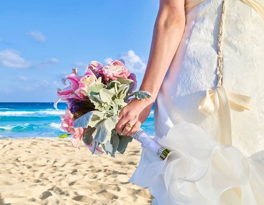 Noiva com buquê de flores na praia. Celebre o seu casamento no Hotel Grand Park Royal Cozumel