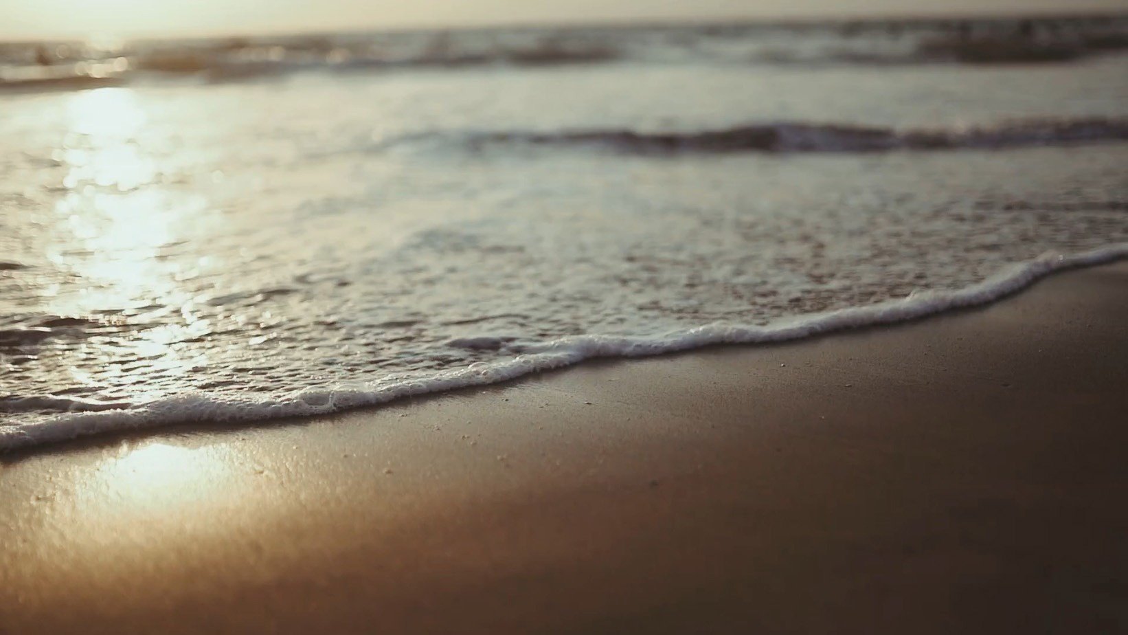 waves crashing on a sandy beach at sunset