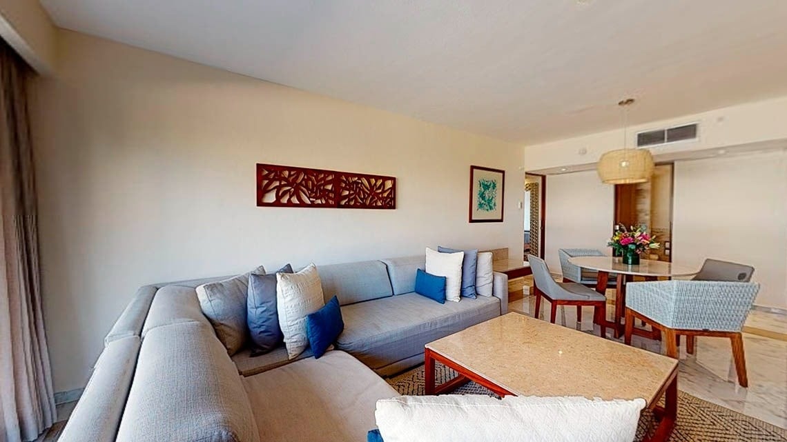 Área de descanso com sofás, mesas e cadeiras em um quarto do Park Royal Beach Cancun Hotel