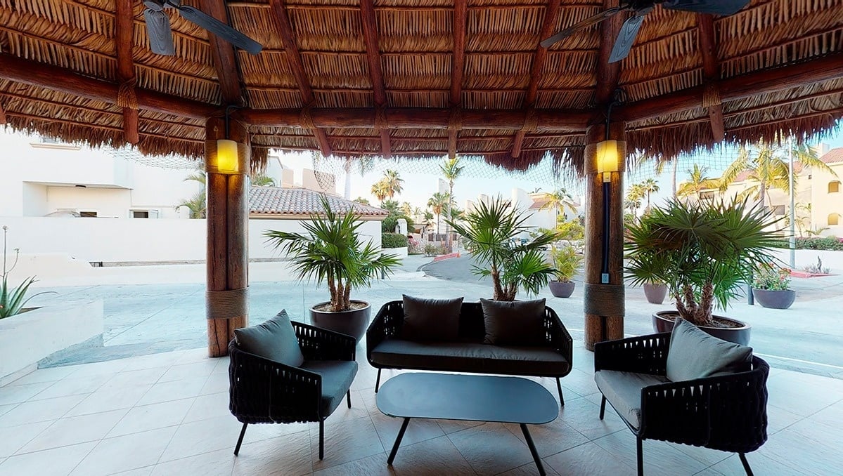 a gazebo with a couch and chairs under a thatched roof