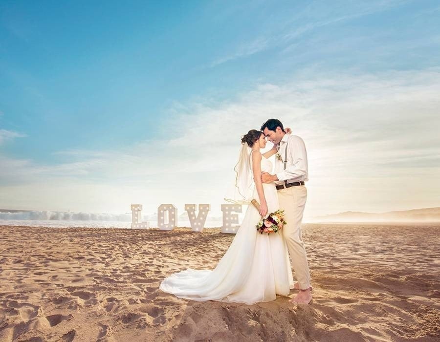 Casal de noivos na praia com letras de lâmpada formando a palavra amor, Park Love por hotéis e resorts Park Royal