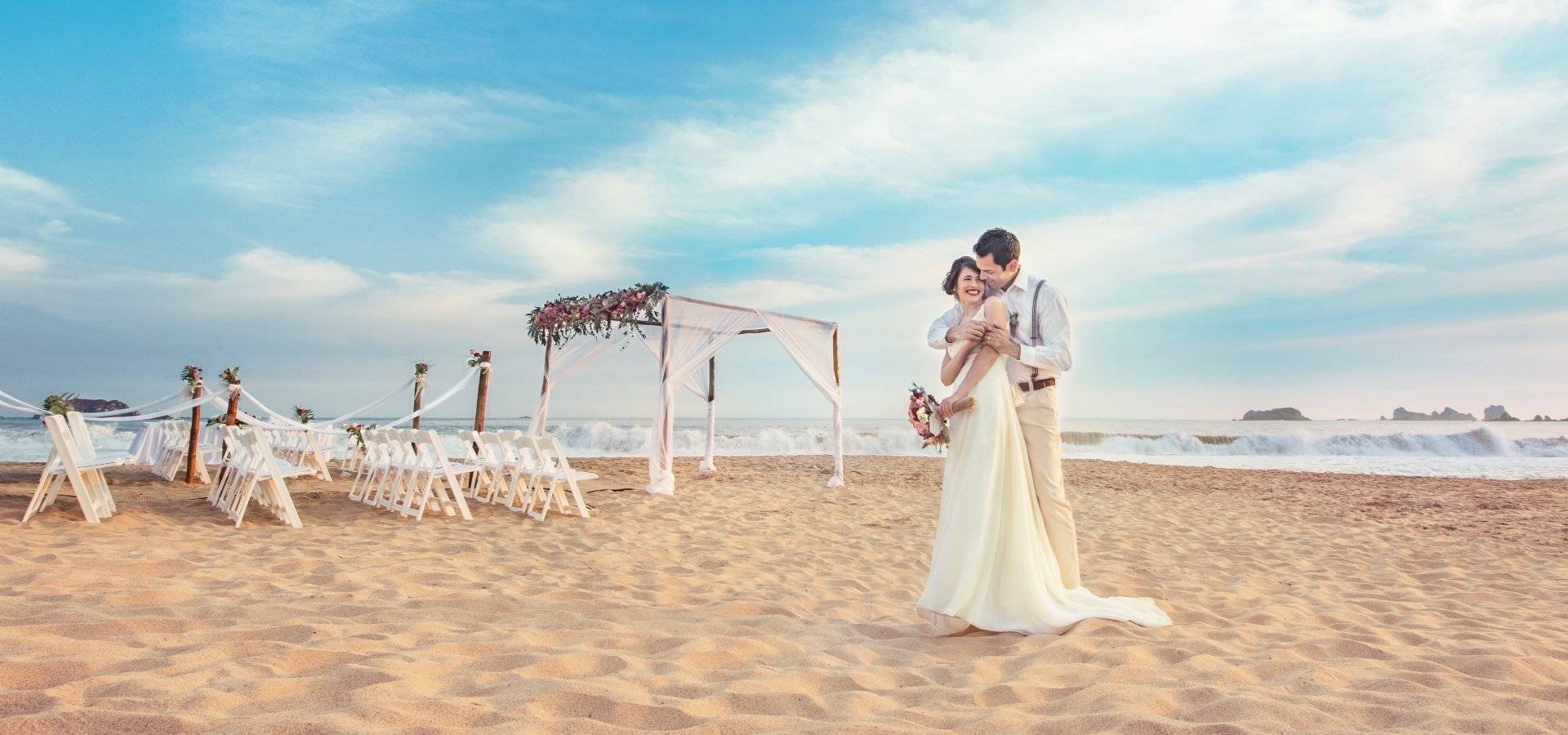 a bride and groom standing on a sandy beach