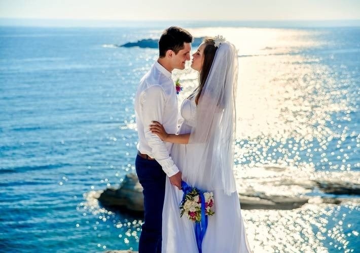 a bride and groom are kissing in front of the ocean