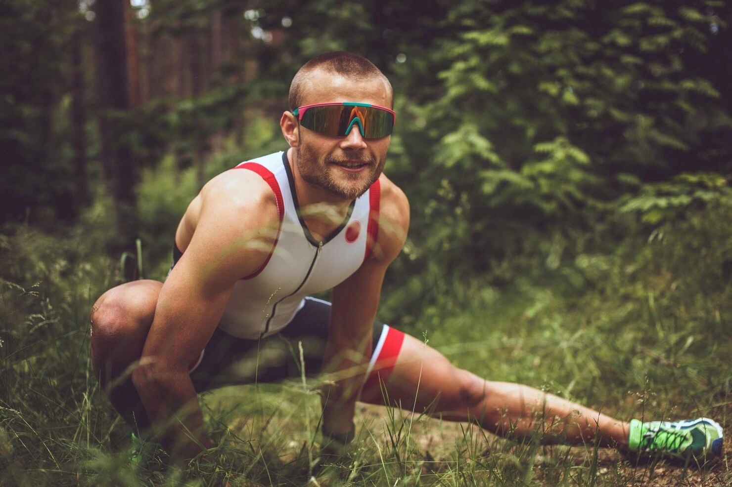 Deportista en Park Royal Hotels & Resorts en México con traje de triatlón y gafas de sol haciendo estiramientos en el bosque.