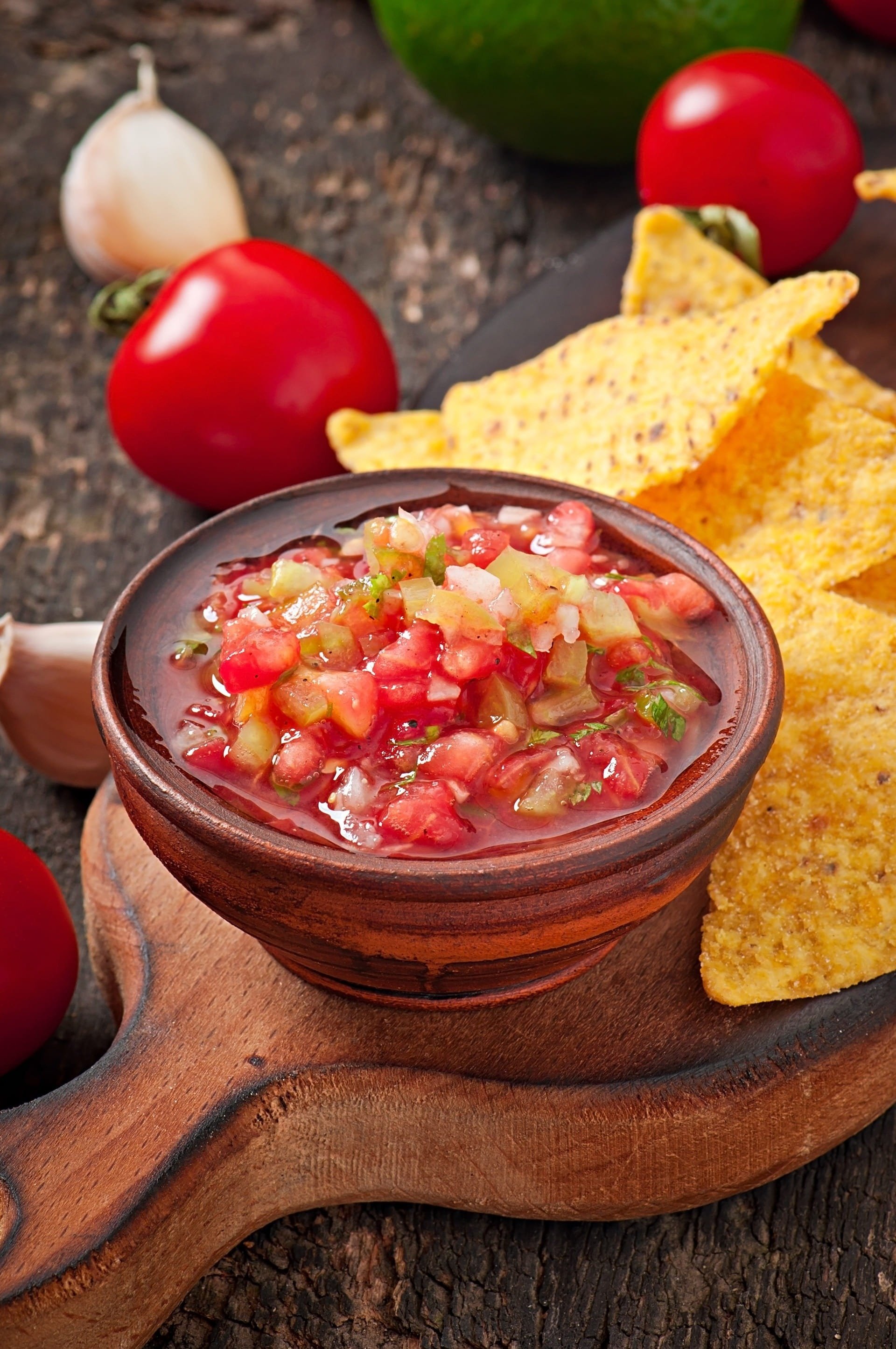 a bowl of salsa sits on a wooden cutting board next to tortilla chips