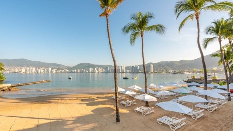 Praia com guarda-sóis, bancos e palmeiras do Hotel Park Royal Beach Acapulco