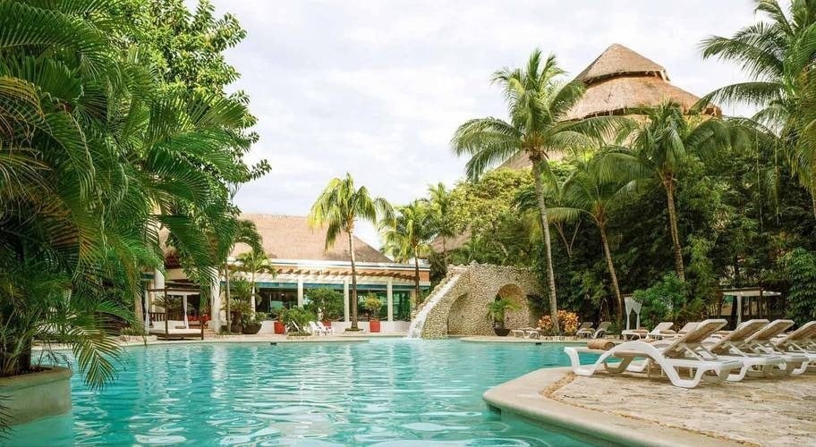 Piscina ao ar livre cercada por árvores tropicais no Hotel Grand Park Royal Cozumel