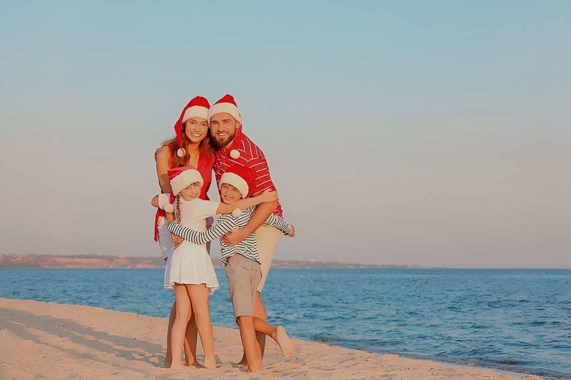 una mujer y un niño están sentados en la playa decorando un pequeño árbol de navidad .