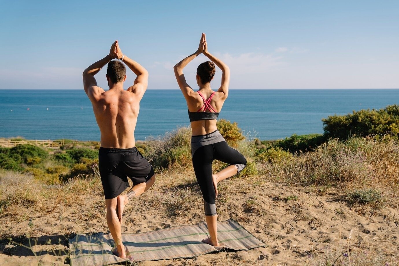 um homem e uma mulher estão praticando yoga na praia