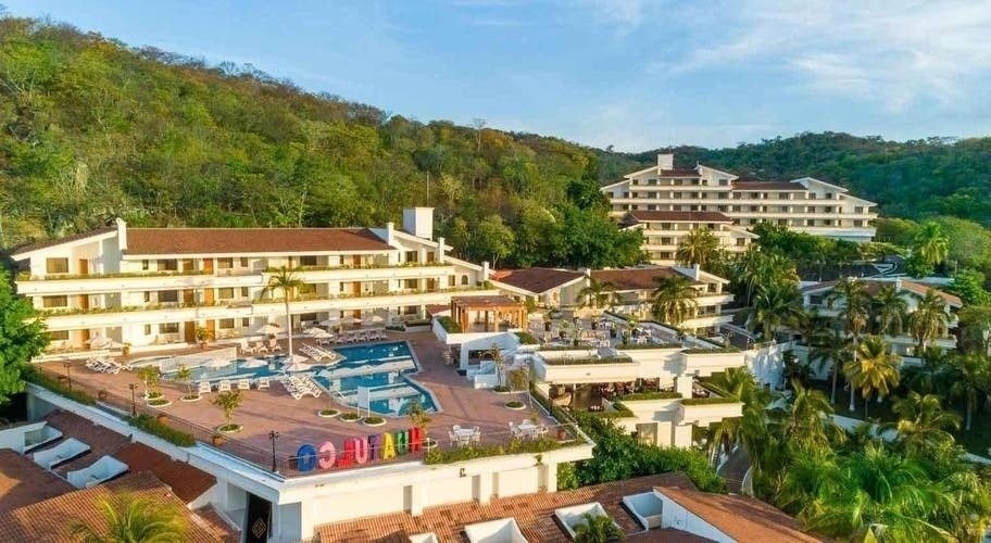 an aerial view of a resort with a large swimming pool surrounded by palm trees