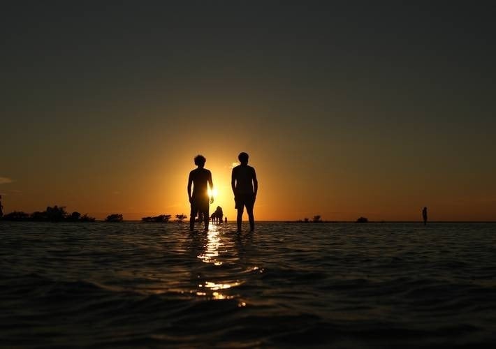 two people standing in the water at sunset